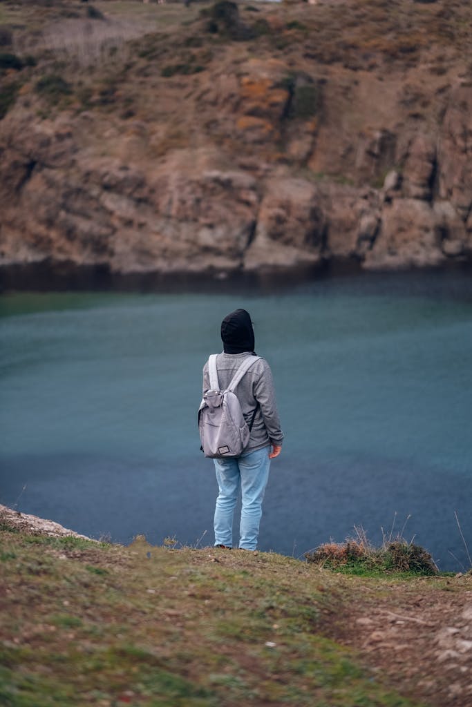 A person with a backpack gazes at a tranquil coastal landscape.